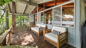 A covered wooden deck with two white sofas and a bench, large windows, and a view of a snowy landscape.