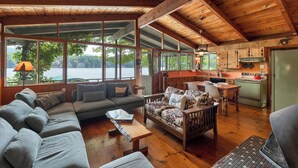 A spacious living area with a large sofa, a patterned sofa, and a dining table. A kitchen with wooden cabinets and a stove is visible in the background.
