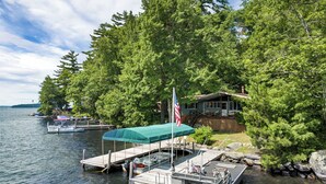 A dock with boats, a covered area, and a house surrounded by trees.