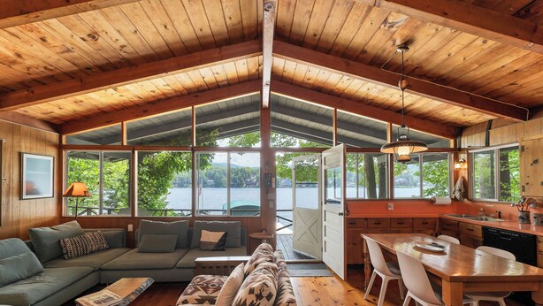 A spacious cabin with a large dining area, a cozy living room with a sofa and a coffee table, and large windows offering a view of the outdoors.