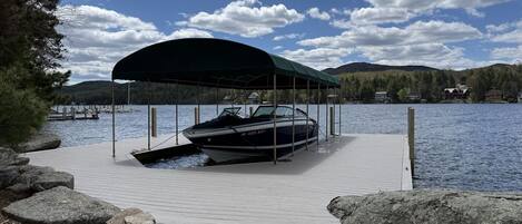 A boat docked under a covered area on a wooden pier with a lake and hills in the background.