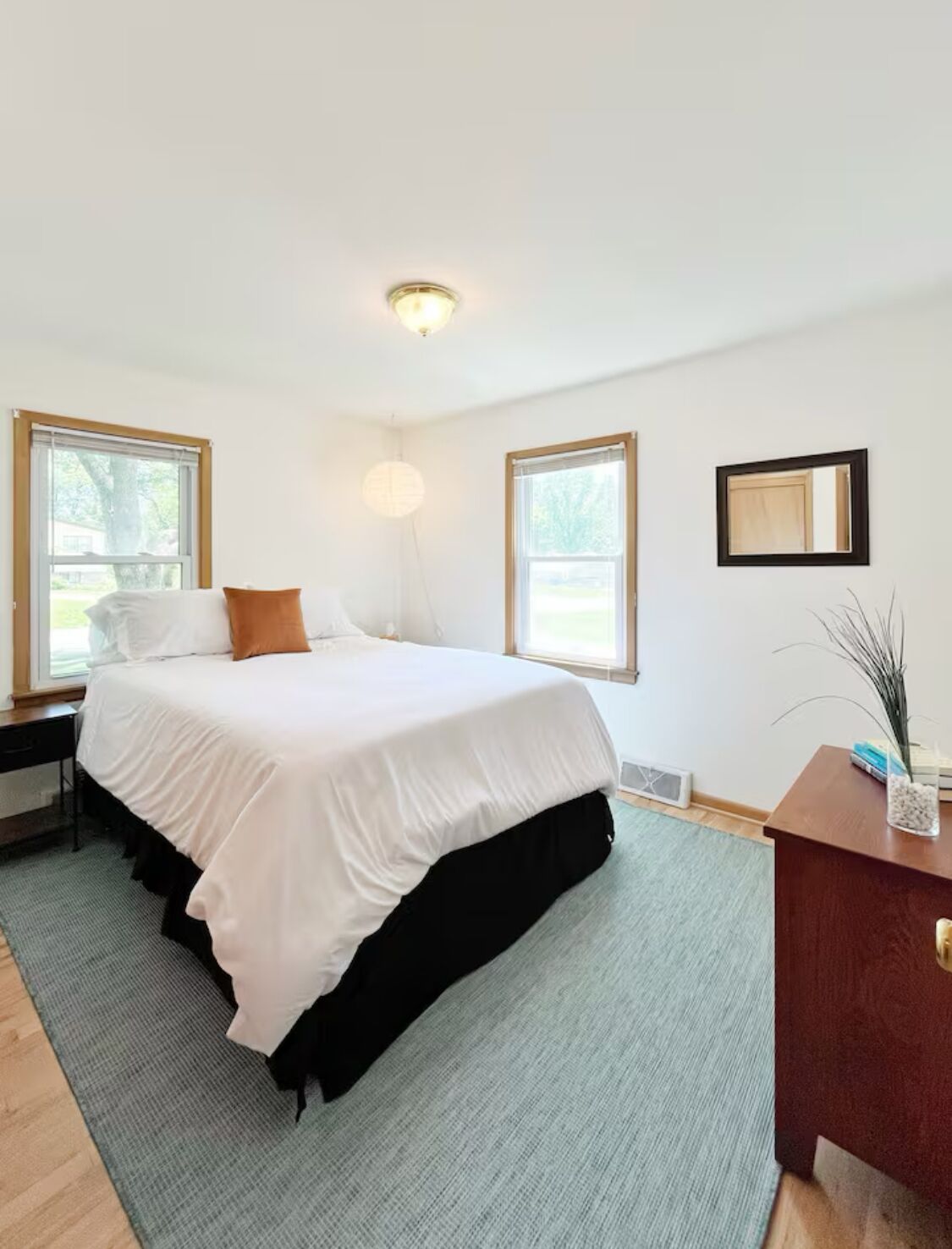 A modern bedroom with a large bed, two windows, a bedside table, and a nightstand.
