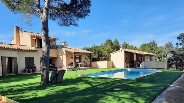 Una propietat residencial amb piscina, gespa verda i dues cases amb teulades de rajola.
