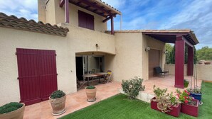 Una casa de dues plantes amb un pati, una zona de menjador i una zona d'estar a l'aire lliure coberta.