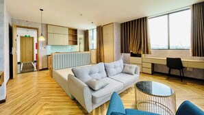 A modern hotel room with a sofa, a small round table, a desk, and a view of the city through large windows. - River View Hotel (Ho Chi Minh City)