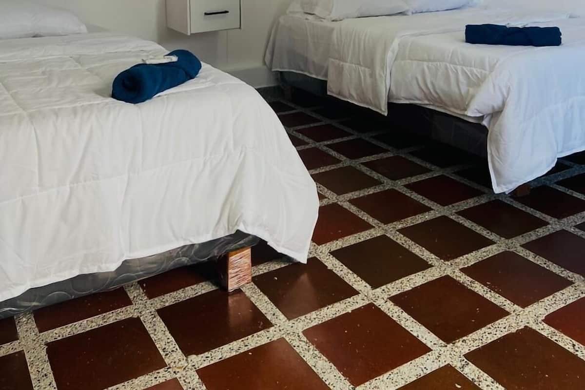 A hotel room with two beds, a small bedside table, and a wall-mounted shelf with decorative items.