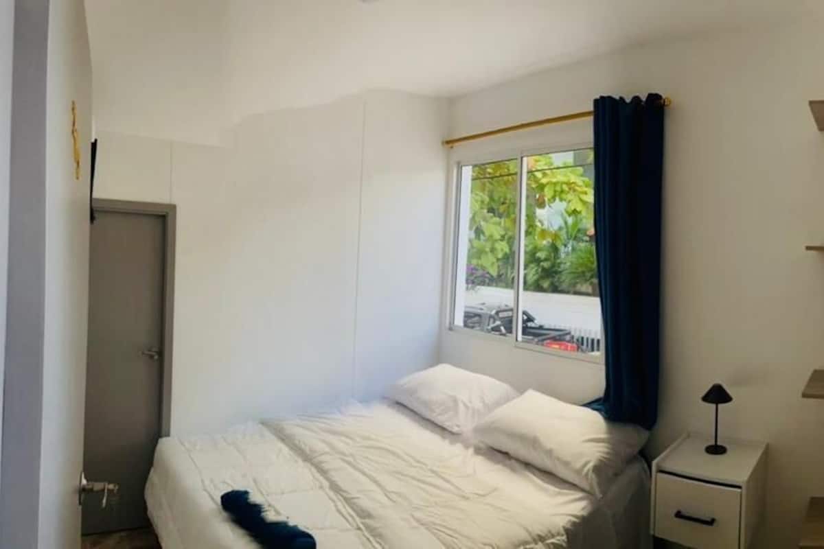 A bedroom with a bed, a nightstand, a lamp, and a window with curtains.