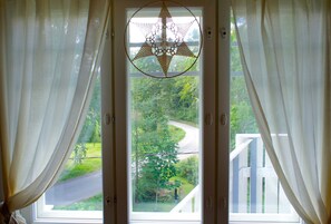 A window with white curtains, a star-shaped hanging ornament, and a view of a winding road through a green landscape.
