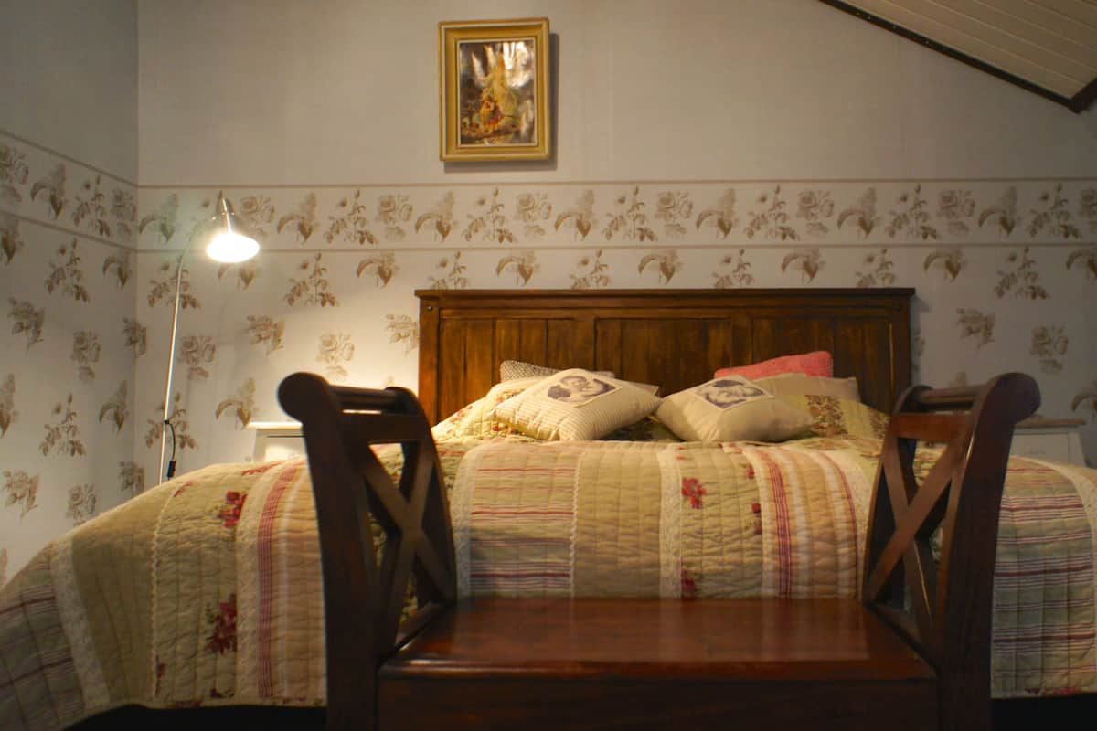 A bedroom with a wooden headboard, floral wallpaper, and a bed with a quilted bedspread.