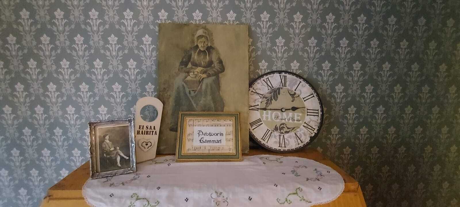A vintage clock, a framed certificate, and a portrait on a table against a patterned wallpaper background.