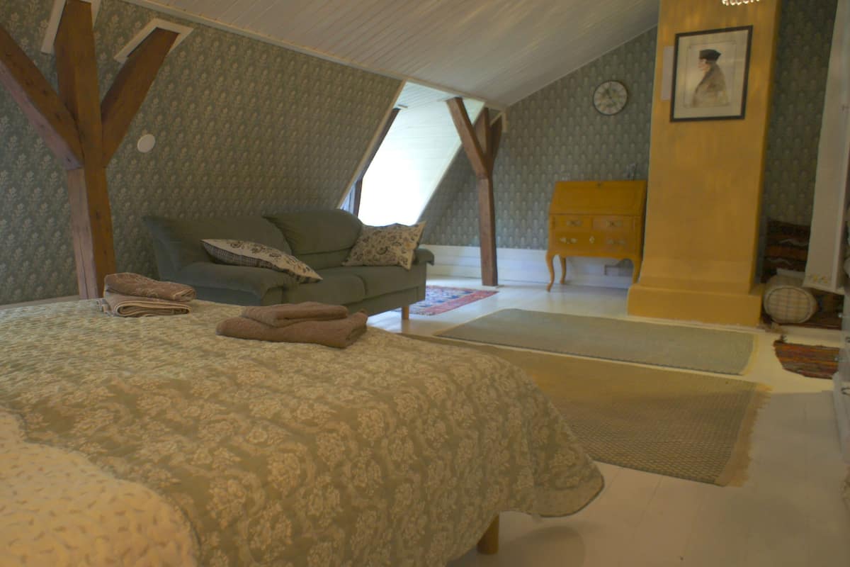 A bedroom with a bed, a sofa, and a wooden chair.