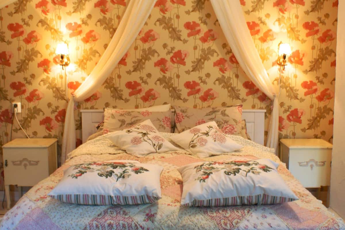 A bedroom with a floral wallpaper, a canopy bed, and bedside lamps.
