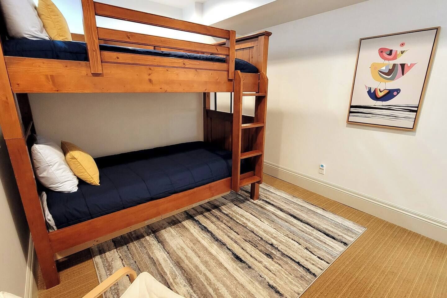 Habitación con literas, una escalera de madera, un colchón azul y una alfombra a rayas.