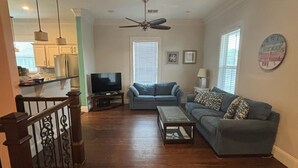 A spacious living room with a wooden floor, a ceiling fan, a blue sofa, and a television.
