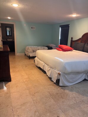 Un dormitorio con cama, cómoda, tocador con espejo y ventana con persianas.