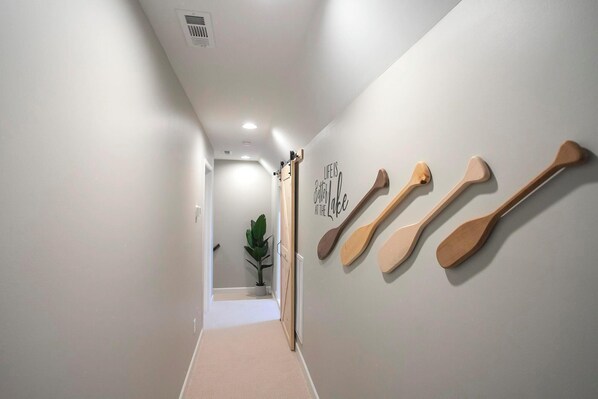 Un couloir orné d’une plante, un mur décoré de pagaies en bois et un panneau indiquant : « La vie est plus belle au bord du lac ».
