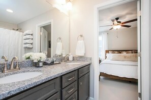 Une salle de bain moderne avec des comptoirs en granit, un grand miroir et un ventilateur de plafond.