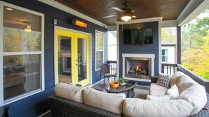 A cozy outdoor living area with a fireplace, comfortable seating, and large windows.