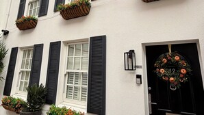 A white building with black shutters, flower boxes on the windowsills, and a black door with a wreath.