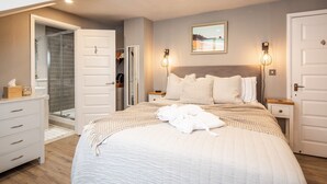 A neatly arranged bedroom with a large bed, bedside tables, a wardrobe, and a shower area.