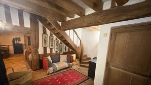 A rustic interior with exposed wooden beams, a staircase, a sofa, and a red patterned rug.