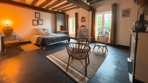 A cozy bedroom with a bed, a small table, two chairs, and a window with curtains.