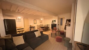 A cozy living room with a sectional sofa, a dining area with a table and chairs, a kitchen with a refrigerator, and a door leading to another room.
