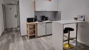 Moderni keittiö, jossa on valkoiset kaapit, mikroaaltouuni, kahvinkeitin ja pieni baaritiski jakkaroineen.