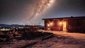 Un edificio rústico con un amplio arco de entrada, ubicado en un paisaje desértico bajo un cielo estrellado.