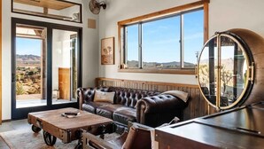 Una habitación con sofá de cuero, mesa de centro de madera y un amplio ventanal con vistas al desierto.