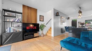 Una sala de estar moderna con un televisor de pantalla plana, una estantería, un sofá azul y una escalera que lleva a otra habitación.