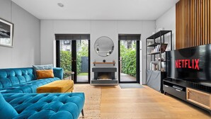 Una sala de estar moderna con un sofá azul, una chimenea y una gran pantalla de televisión que muestra el logo de Netflix.