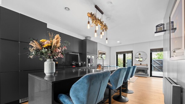 Una cocina moderna con armarios oscuros, una isla central con taburetes y un arreglo floral decorativo.