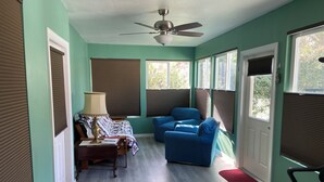 Una habitación con ventilador de techo, una cama con colcha, un sillón azul y una alfombra roja.