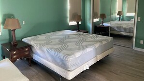 Un dormitorio con cama, dos mesitas de noche con lámparas, cómoda, espejo y ventana con persianas.