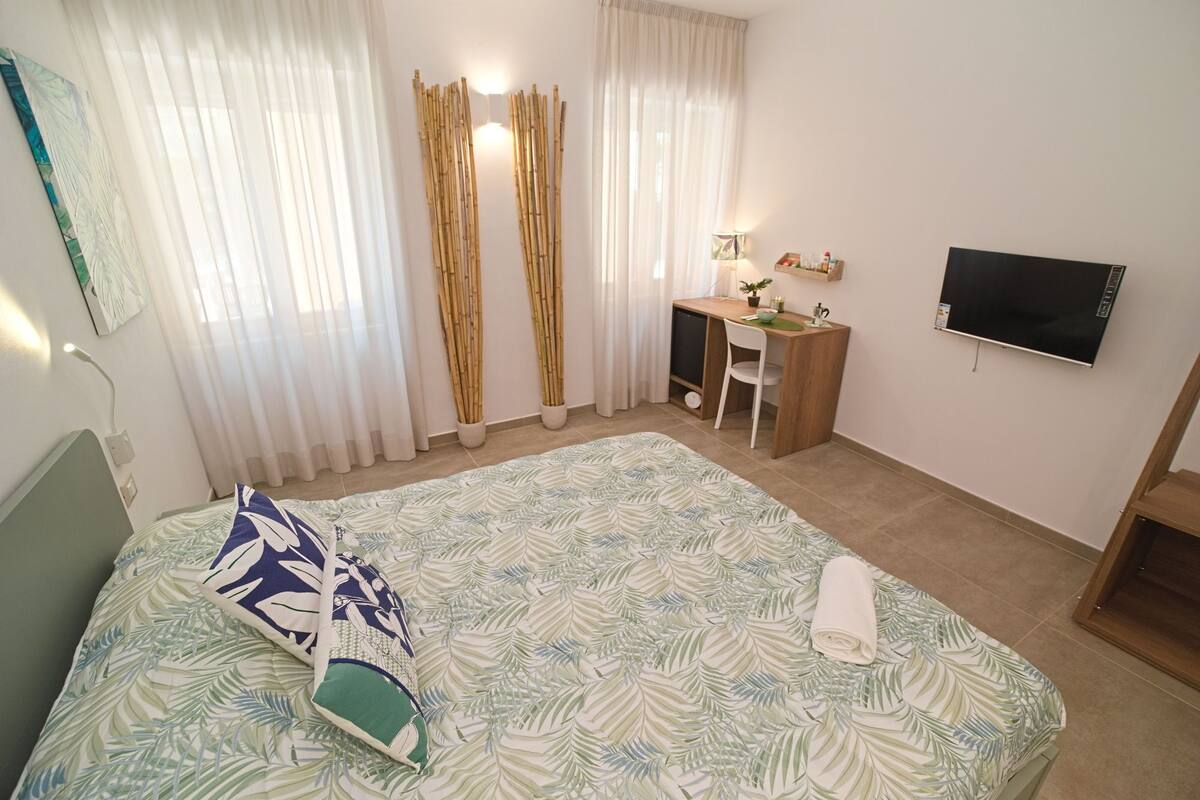 Ein Hotelzimmer mit Bett, Schreibtisch, Stuhl, Fernseher und einem Fenster mit Vorhängen.