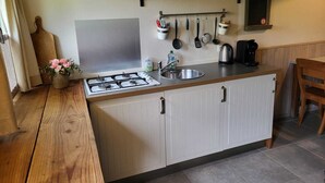 Angolo cottura compatto con fornello a gas, lavello e macchina del caffè. Utensili pensili e piccolo ripiano con barattoli.