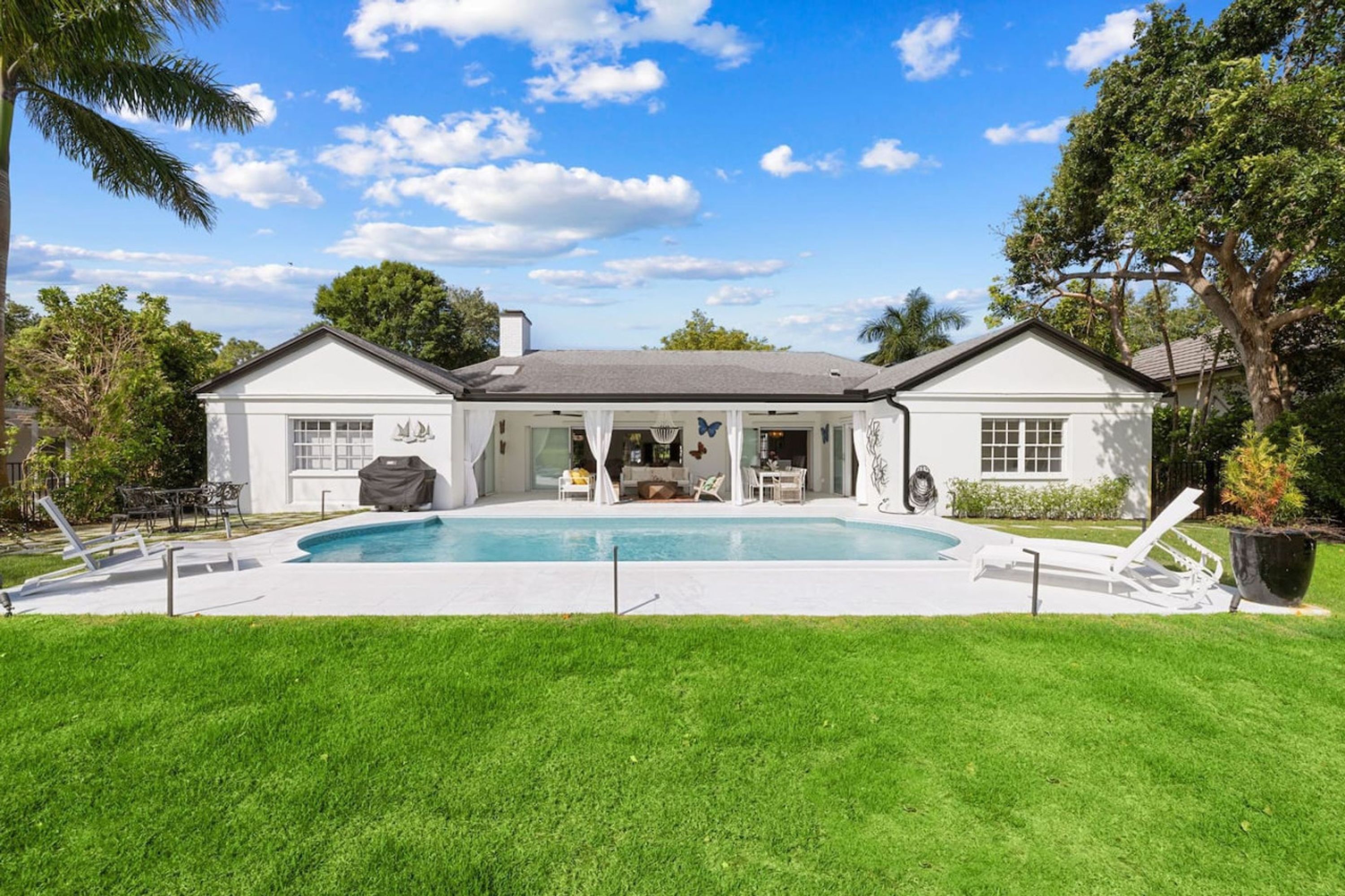 A two-story house with a swimming pool, a covered patio, and a well-maintained lawn.
