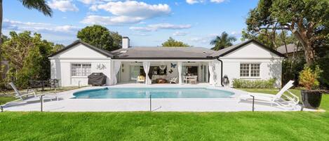 A two-story house with a swimming pool, a covered patio, and a well-maintained lawn.