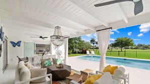 Un espace extérieur abrité avec une piscine, des meubles blancs et un ventilateur de plafond.
