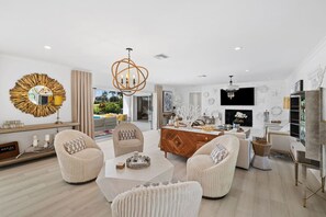 A spacious living room with a central coffee table, two armchairs, and a sofa. A wooden dining table is set with decorative items.
