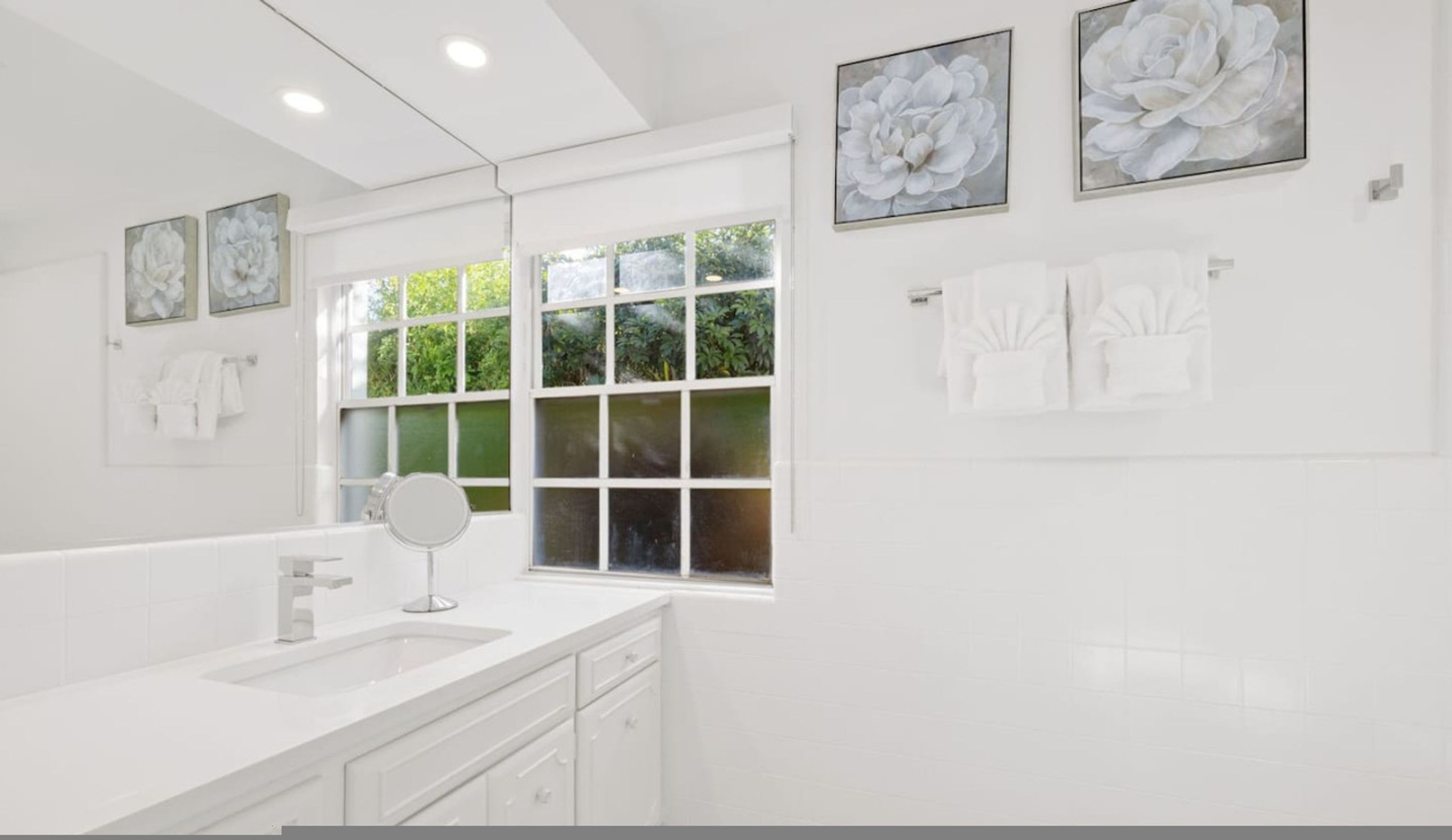 A modern bathroom with a large mirror, white fixtures, and artwork on the walls.