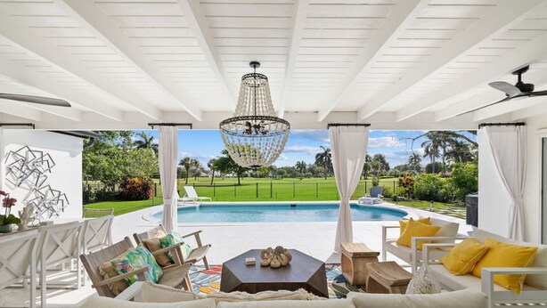 Une terrasse extérieure avec une piscine, des meubles blancs et une vue sur un terrain de golf.
