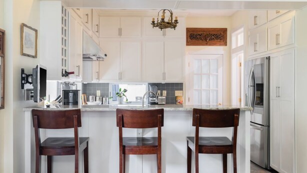 Une cuisine moderne avec des meubles blancs, un îlot central doté de tabourets, des appareils en acier inoxydable et un lustre.