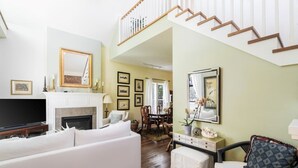 Un salon spacieux avec un canapé blanc, une cheminée, un téléviseur et un escalier menant à l’étage supérieur.