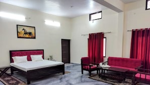 Una habitación de hotel con cama, un sofá rojo, una mesita y un cuadro en la pared.