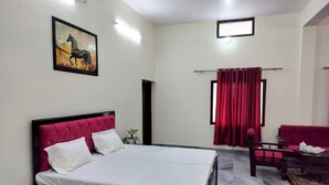 Un dormitorio con cama, sofá rojo, una mesita y cortina roja, además de un cuadro en la pared.