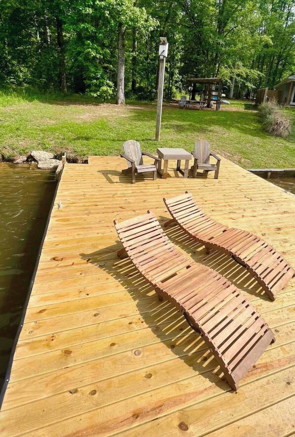 A wooden deck with lounge chairs and a table, overlooking a body of water.