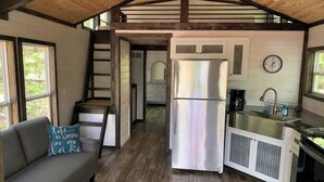 A compact kitchen with a stainless steel refrigerator, a sink, and a clock on the wall.