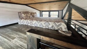 A bedroom with a bed, wooden flooring, a sloped ceiling, and a window.